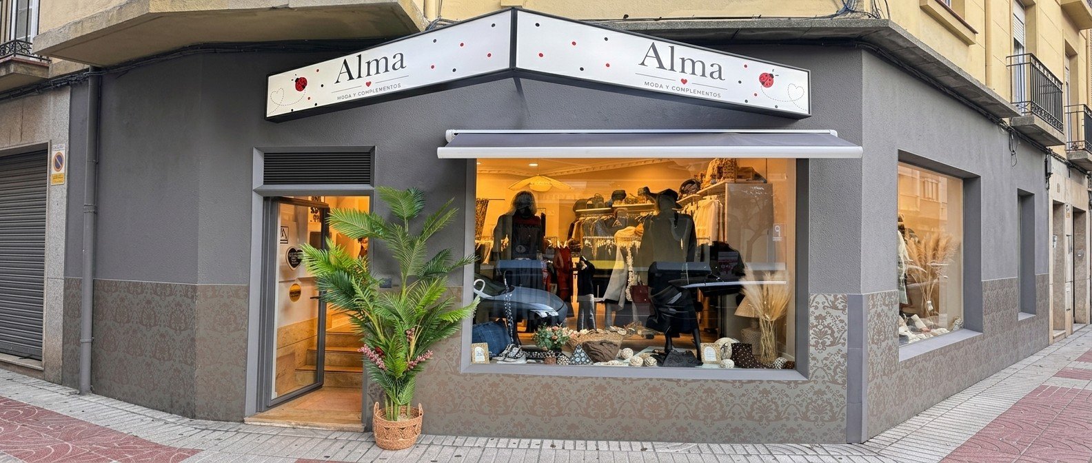 Fachada de Alma en esquina, pintada en gris, con escaparate iluminado y rótulo blanco